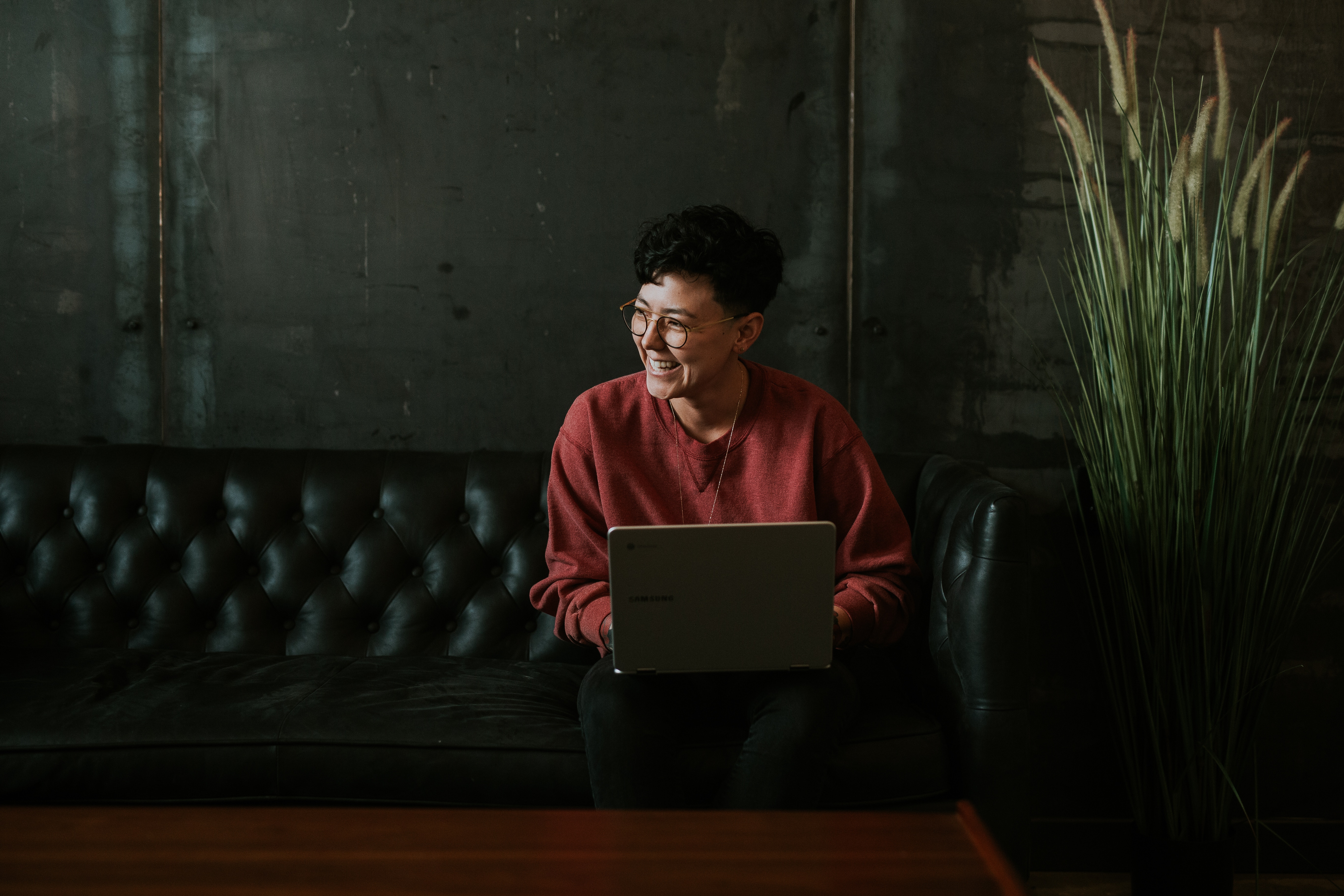 woman with glasses laughing while sitting on the couch photo by Brooke Cagle via Unsplash